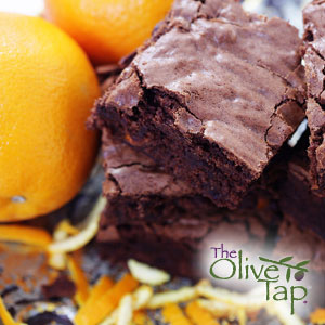 Stack of chocolate brownies with a crackly top, surrounded by fresh oranges and orange zest, creating a decadent chocolate-citrus dessert display.