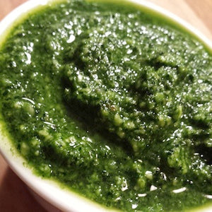 A bowl of green kale garlic walnut pesto sauce with a smooth texture and a glossy olive oil finish.