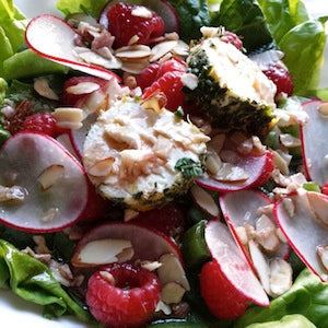A bed of leafy greens, topped with sliced radishes, raspberries, sliced almonds, and herb goat cheese.