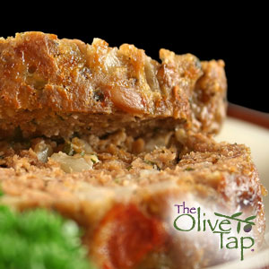 Two stacked pieces of meatloaf on a white plate with a green garnish against a black background.