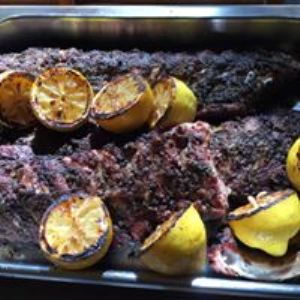 Grilled ribs with grilled halved lemons in a metal container.