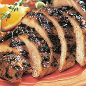 Sliced jerk chicken breast with a dark crust, served on an orange plate with an orange wedge.