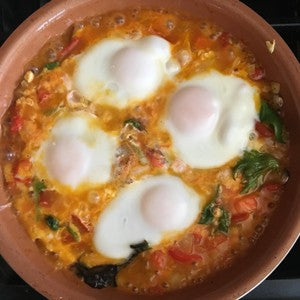 Poached eggs, tomatoes, peppers, and leafy greens cooked in a skillet.