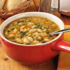 White bean and kale soup with vegetables served in a red bowl with a spoon.