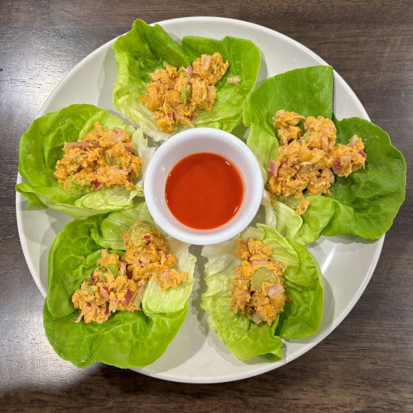 Five crisp lettuce cups filled with chickpea salad, arranged around a small bowl of red dipping sauce on a white plate.