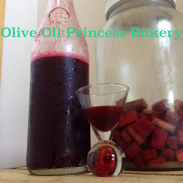 A bottle and glass of deep red beverage beside a jar filled with chopped rhubarb pieces.