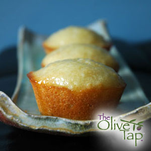 Three muffins with a citrus glaze lined up on a blue decorative plate and The Olive Tap logo in the righthand bottom corner.