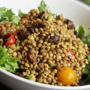A salad topped with lentils, cherry tomatoes, and kalamata olives, served in a white bowl.