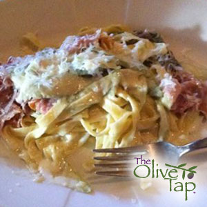 Fresh pasta topped with a goat cheese and prosciutto sauce on a white plate with a fork.