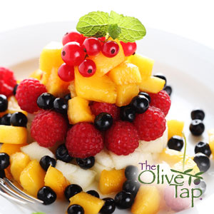 Colorful fresh fruit salad layered with mango, pineapple, raspberries, blueberries, red currants, and melon, garnished with a sprig of mint and served on a white plate.