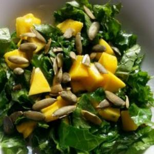 Kale salad topped with mango pieces and sunflower pepitas, served in a white bowl.