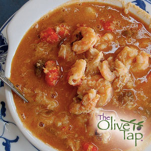 A bowl of gumbo with shrimp, sausage, tomatoes, and rice in a rich broth, served with a spoon.