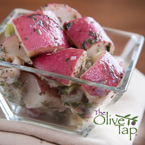 Herb-marinated red potato salad featuring chunks of red-skinned potatoes tossed with herbs and a light vinaigrette, served in a clear glass dish.