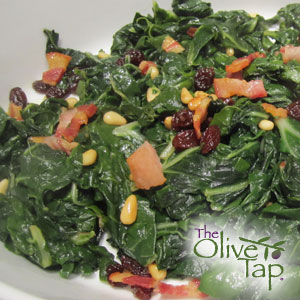 Braised swiss chard with pine nuts, pancetta, and raisins on a shallow white dish.