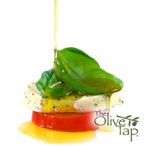Classic Caprese stack featuring fresh mozzarella, tomato, and basil, drizzled with golden olive oil and sprinkled with herbs, served against a white background.