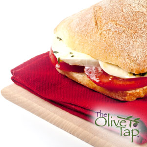 Fresh Caprese sandwich made with sliced mozzarella, ripe tomatoes, and basil on a crusty artisan roll, served on a wooden board with a red napkin.