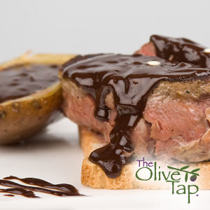 Sliced steak with a pink center, topped with a dark chocolate sauce and served on toasted bread beside a potato also covered in sauce..