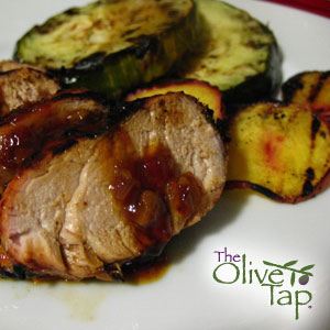 Sliced pork tenderloin drizzled with a savory glaze, served alongside grilled zucchini on a white plate.