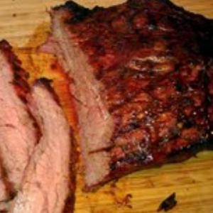Sliced flank steak with a seasoned crust served on a wooden cutting board.