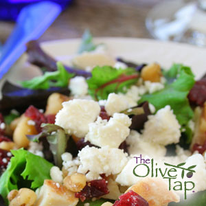 Mixed greens salad topped with feta cheese crumbles, pomegranate seeds, and walnuts, served on a white plate. 