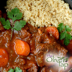 Hearty lamb stew featuring tender chunks of lamb and carrots simmered in a rich brown gravy, served alongside fluffy couscous and garnished with fresh parsley.