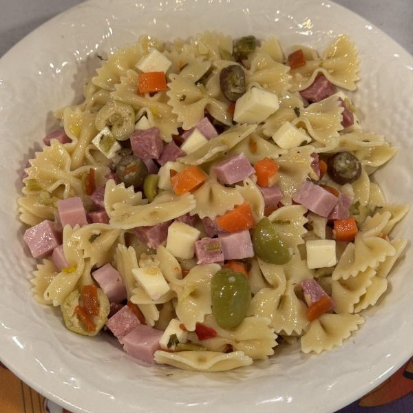 Bowtie pasta with olives, ham, salami, and cheese, served in a white bowl.