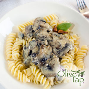 Rotini pasta topped with a creamy mushroom sauce made with sliced mushrooms and herbs, garnished with a fresh basil leaf and served on a white plate.