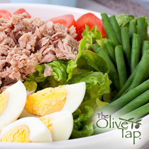 A close-up of a salad with tuna, cherry tomatoes, green beans, lettuce, and cut hardboiled eggs in a white bowl.
