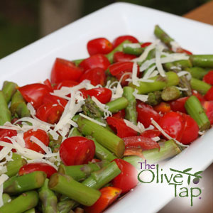 Fresh asparagus and tomato salad made with crisp asparagus pieces, cherry tomatoes, shredded Parmesan cheese, and herbs, served on a white platter.