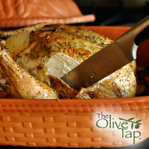 Herb-roasted whole chicken with golden, crispy skin being carved in a baking dish.