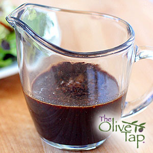 A glass pitcher of strawberry vinaigrette on a wooden surface.