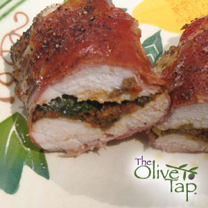 Two baked chicken breasts stuffed with a tapenade and wrapped in prosciutto on a decorative plate and The Olive Tap logo in the righthand corner.