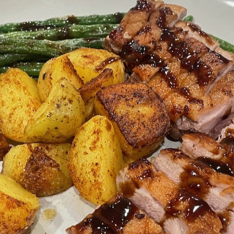 Pan seared duck with a Black Currant reduction sauce and a side of roasted duck fat potatoes and green beans on a white plate.