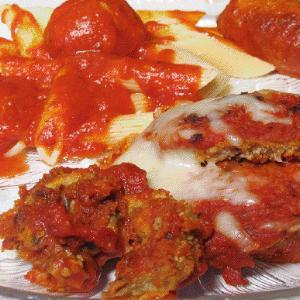 Breaded chicken cutlets topped with tomato sauce and melted cheese, served with penne pasta and tomato sauce on a plate.