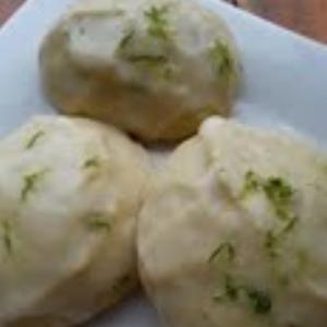 Three light-colored olive oil cookies topped with lime zest and served on a white plate.
