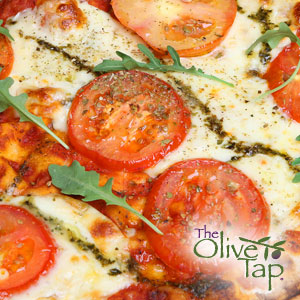 A close up of a pizza with cheese, tomato slices, fresh arugula, and oil drizzles.