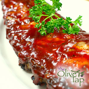 Barbecue pork ribs coated in a glossy, caramelized barbecue sauce and garnished with fresh parsley, served on a white platter.