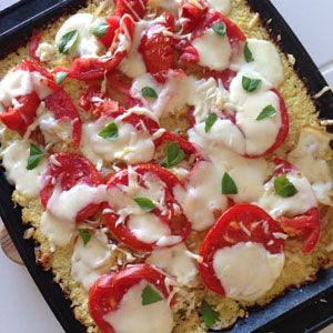 Pizza with cauliflower crust topped with fresh tomatoes, mozzarella cheese, and chopped basil.