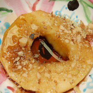 Poached apple slice drizzled with balsamic walnut glaze and topped with chopped walnuts, served on a colorful plate.