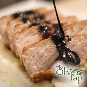Sliced pork tenderloin being drizzled with a dark pomegranate sauce on a bed of white mashed vegetable.