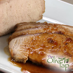 Sliced pork tenderloin drizzled with a molasses, bacon, and porcini vinaigrette on a white plate.