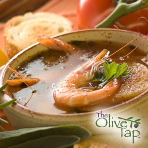 A soup with shrimp prawns in a bowl in front of fresh bread and a tomato on a vine.