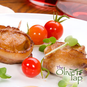 Scallops wrapped in prosciutto on a white plate with cherry tomatoes and garnished with micro greens.