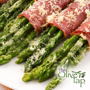 A plate of bundles of asparagus wrapped in proscuitto topped with grated parmesan on a white plate.