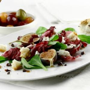 Watercress and radicchio salad topped with figs and cheese crumbles, topped with hazelnut pieces.