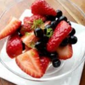 A bowl of mixed berries with sliced strawberries and blueberries, topped with fresh mint and served in a white dish.
