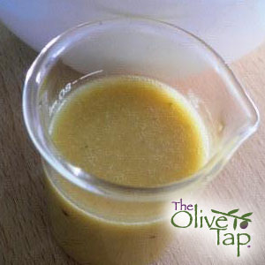 Small glass pitcher filled with creamy honey vinaigrette dressing, served on a wooden surface.