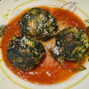 Three large spinach and ricotta gnocchi served over a red tomato sauce and topped with a sprinkle of grated parmesan cheese.