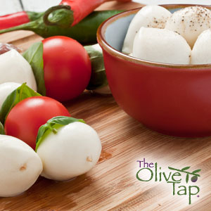 A bowl of fresh mozzarella balls sprinkled with pepper and skewers with mozzarella balls, fresh basil, and tomatoes on a wooden surface.