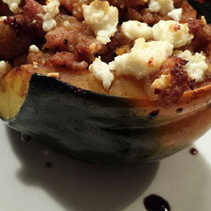 Half of an acorn squash stuffed with a meat mixture, topped with feta cheese, and drizzled with a balsamic glaze.